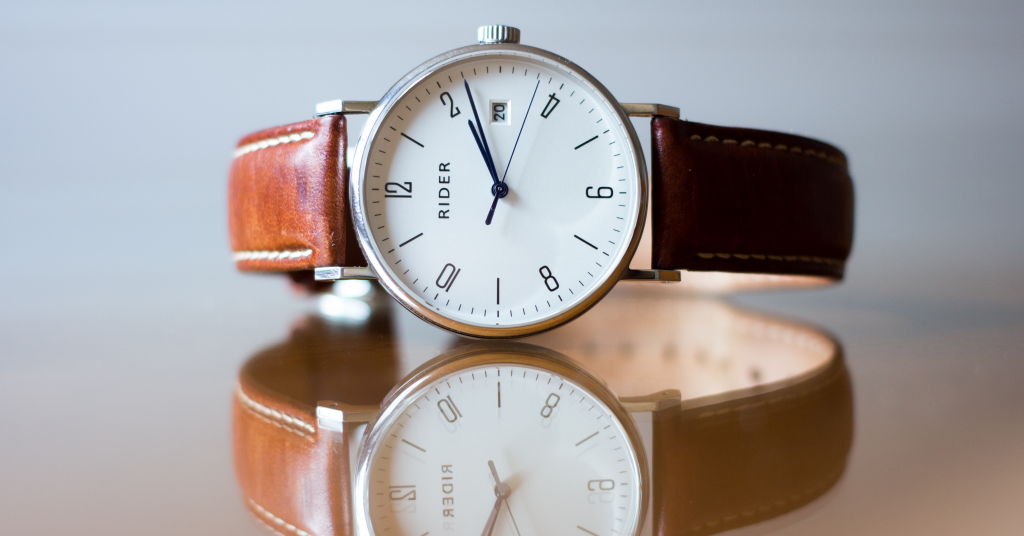 Brown leather watch with a white face and silver hands, sitting on a wooden surface.