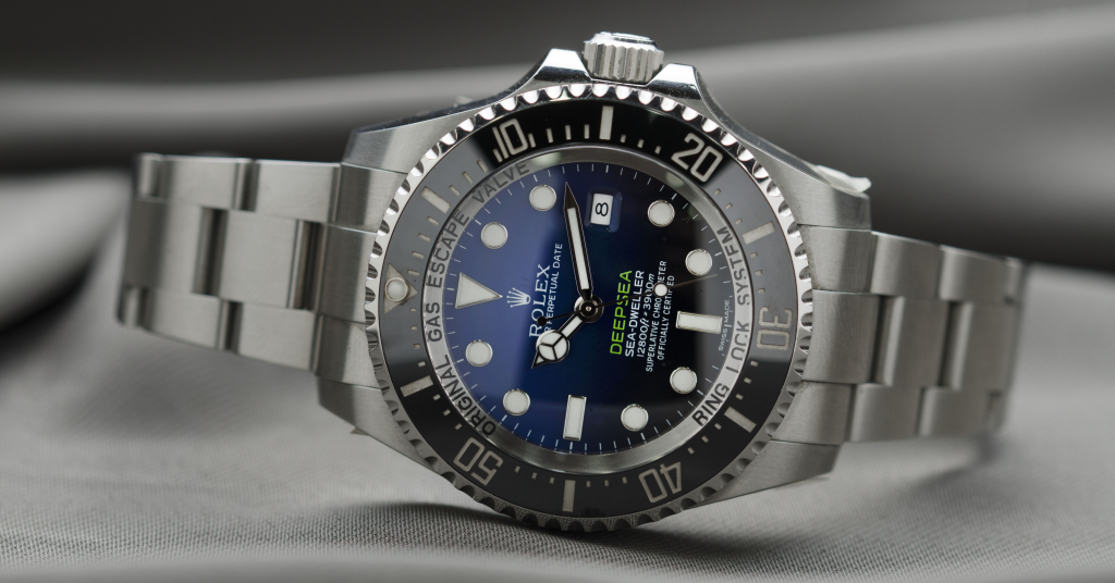 Rolex watch with a Black face and silver hands, sitting on a grey board surface.